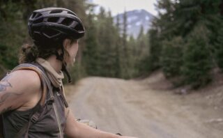 Woman in sleeveless riding top and bike helmet peering down fire road at mountain in the distance.